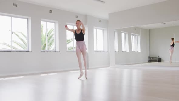 Caucasian female ballet dancer practicing ballet during a dance class in a bright studio