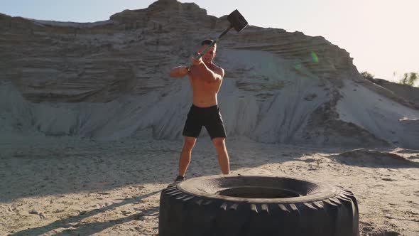 Muscle Athlete Strongman Man Hits a Hammer on a Huge Wheel in the Sandy Mountains in Slow Motion