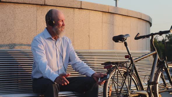 Elderly Pensioner in Headphones Sits on Bench Next Bike Listens Melody Resting After Trip Enjoying