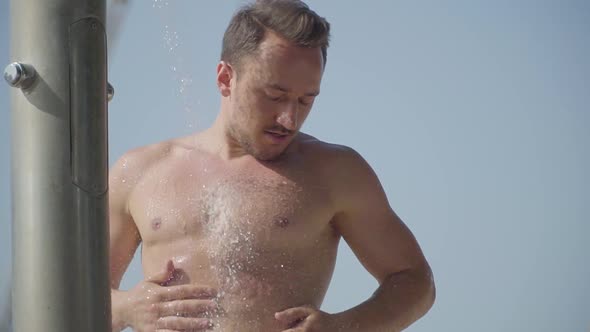 Attractive Athletic Man Washing Under the Water in the Beach Shower Outdoors