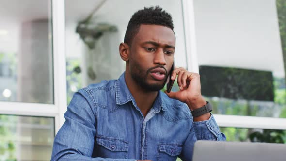 African american businessman talking on smartphone and using laptop outisde cafe cmmunication, busin