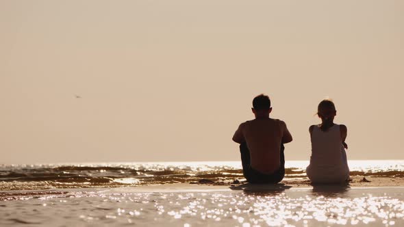 A Man and a Woman Sit Side By Side on the Beach