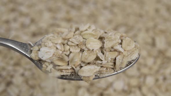 Uncooked raw oatmeal falls into a full spoon in slow motion