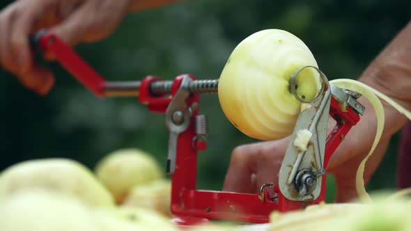 Female Hands Peeling a Green Apple with an Apple Peeler Outdoors