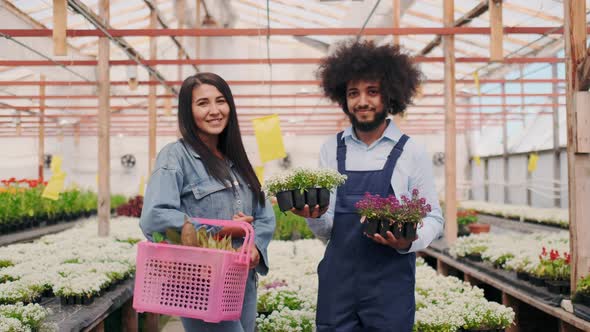 Friendly Curly Latin American Man in Garden Uniform and Pretty Asian Girl Customer with Shopping