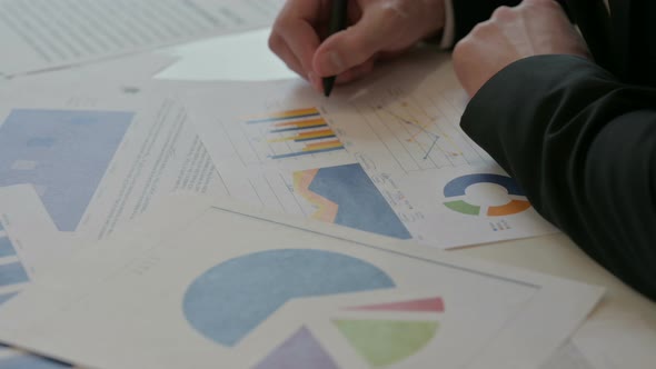 Close Up of Middle Aged Businessman Studying Charts While Holding Pen