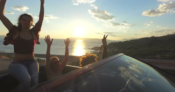 Beautiful brunette sitting on hood of convertible riding with her friends