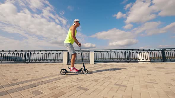 Slow Motion of a Handicapped Man Riding a Scooter Along the Quay