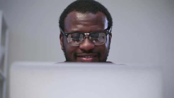 African Man with Glasses and Beard Looks at Laptop Closeup and Smile Spbas