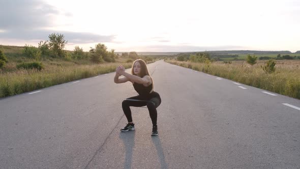 Attractive Girl Training Squats with Fitness Elastic Band on Road at Nature