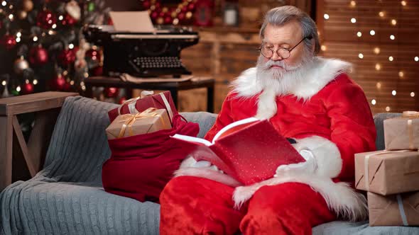 Surprised Male in Santa Claus Costume Reading Christmas Wish List in Red Book