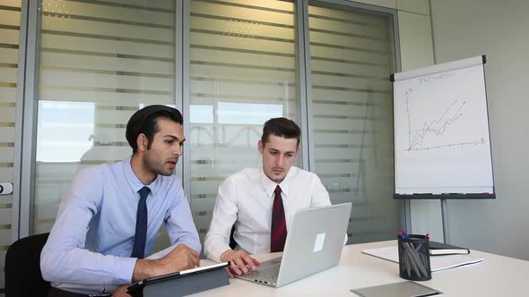 two young business man indoor office interior using personal computer and digital tablet, discussing