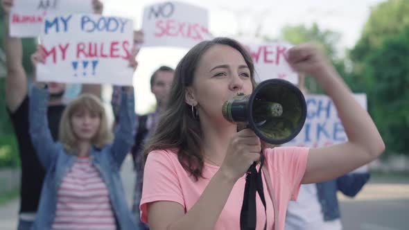 Portrait of Feminist Activist Shouting Through Megaphone with People Shaking Banners at the