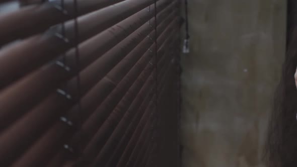 Young Woman Open Blinds on Windows and Looking Out Window Through Blinds