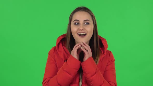 Portrait of Lovely Girl in a Red Down Jacket Is Daydreaming and Smiling Looking Up. Green Screen