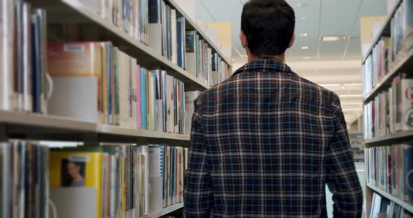 College Student Goes in the Library and Stops to Select a Book