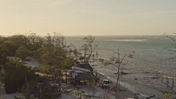 Crane view of trucks driving toward kite surfers in sunset backdrop; drone