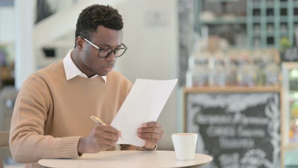 African American Man Reading Documents While Drinking Coffee in Cafe