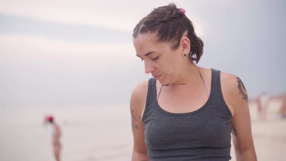 Ordinary Woman 35 Years Old with Dark Hair Tattoos in a Swimsuit Stands on the Beach