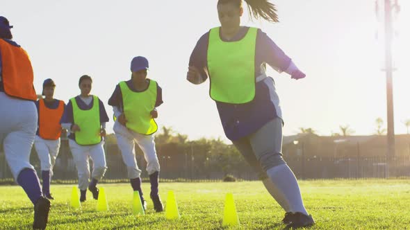 Diverse group of female baseball players exercising on pitch, running between cones