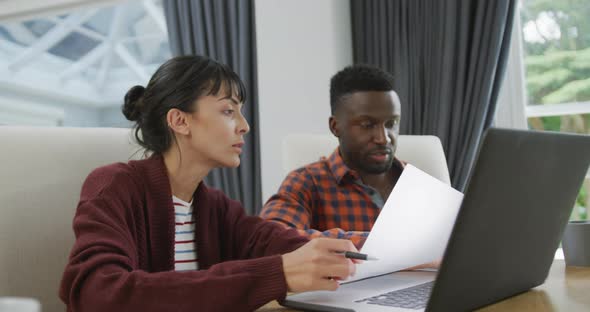 Happy diverse couple sitting at table and working with laptop