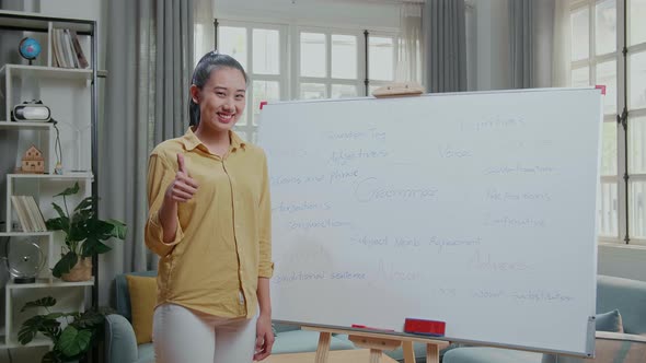 Smiling Asian Female Teacher Showing Thumbs Up Gesture To Camera While Teaching English At Home