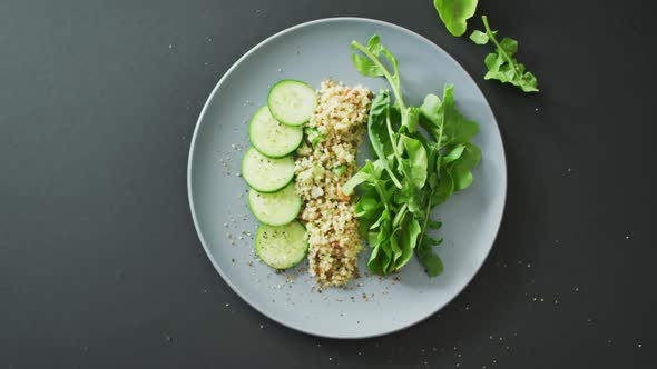 Video of fresh sliced cucumber, leaves and grains salad on grey plate over dark grey background