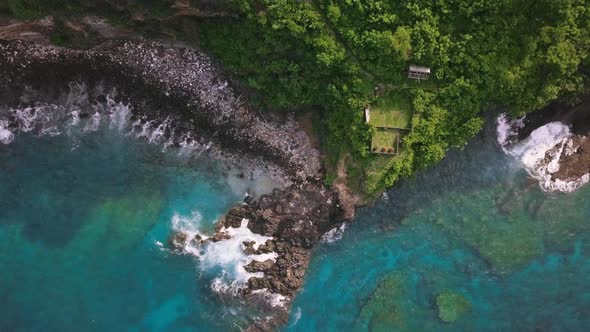 Aerial Top Down View of Rocky Coastline with Green Cliffside and Blue Sea.