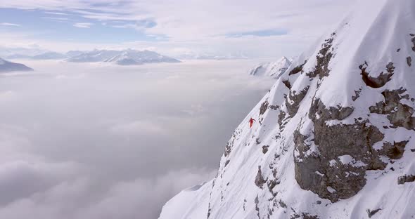 Aerial drone view of a skier skiing down a steep snow covered mountain