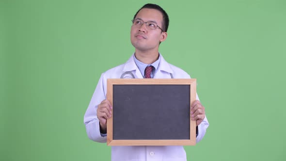 Happy Asian Man Doctor Thinking While Holding Blackboard