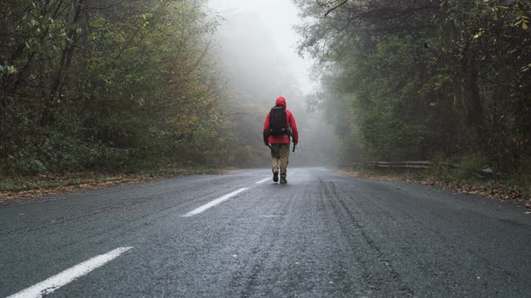 Lonely, Lost Tourist with Black Backpack Walks on Empty Asphalt Road