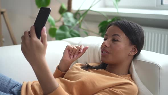 African Woman Lies on Couch and Holds Phone in Hands While Talking Spbd