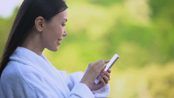 Joyful Woman in White Bathrobe Scrolling Smartphone Photos