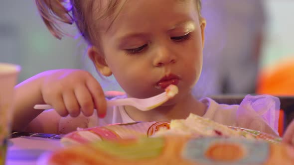 Cute Little Girl Eating a Piece of Cake on a Paper Plate with a Plastic Fork