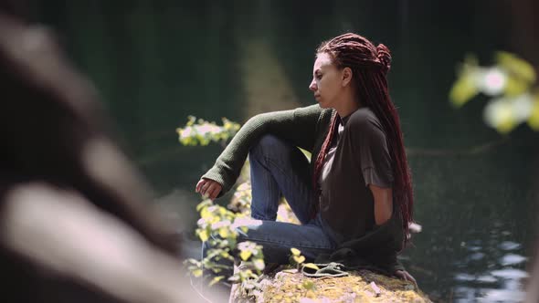 girl sits on the shore of a lake in a dense coniferous forest. loneliness concept