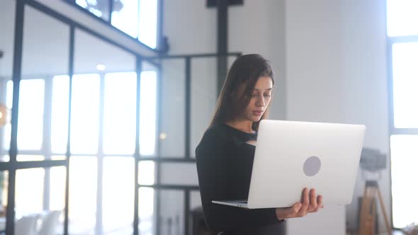 Young Woman Holding Laptop in Hands and Browsing Internet at Home