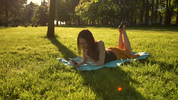 Female Laying Down Over Green Grass While Typing a Message on Phone