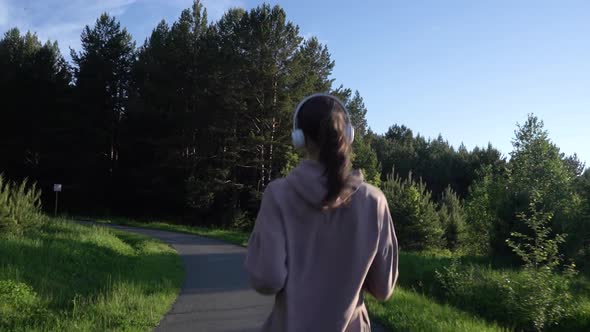 A Girl Jogs in the Park and Listens to Music on Headphones