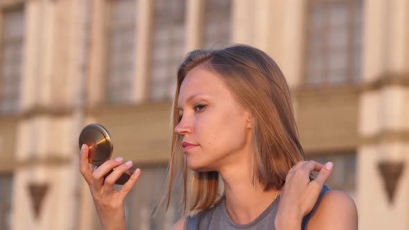 European Girl Blonde Hair Sitting on Bench and Looking in the Mirror.