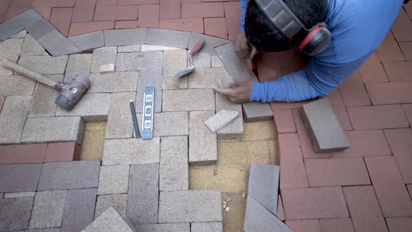 Looking straight down onto the artisan fitting a small wedge of brick into a hardscape design, he pu