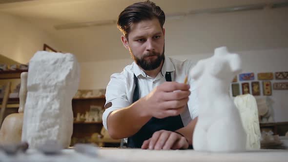 Sculptor Looking at Original Sculpture Making Marks on Future Sculpture at His Workplace