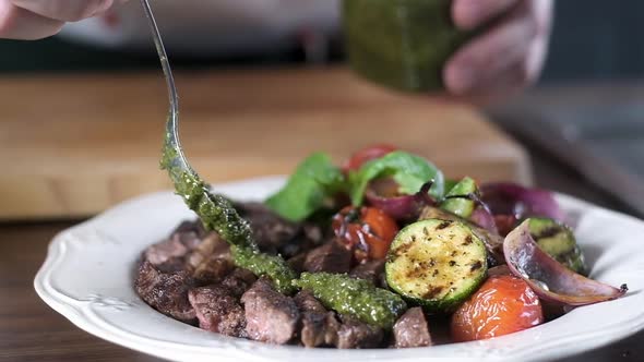 chef pours slices of grilled steak with grilled vegetables with pesto sauce.