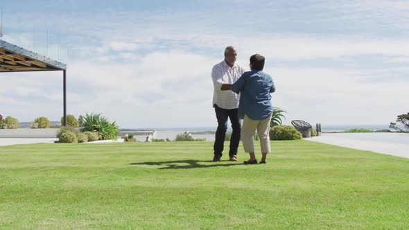 Happy senior diverse couple dancing in garden at retirement home