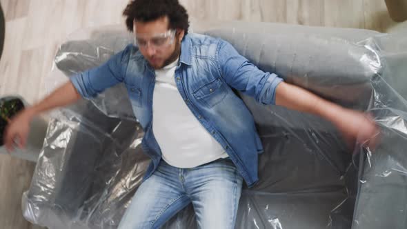 AfroAmerican Man Falls Down on Sofa Covered with Plastic