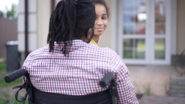 Happy Teenage African American Girl Hugging Disabled Man in Wheelchair Smiling Looking at Camera