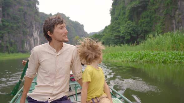 A Young Man and His Son on a Boat Having a River Trip Among Spectacular Limestone Rocks in Ninh Binh