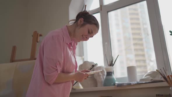 Caucasian Woman Artist Working on a Painting in Bright Daylight Studio