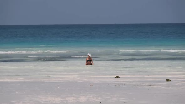 Young Woman in a Black Swimsuit Walks Into the Turquoise Ocean on Paradise Beach