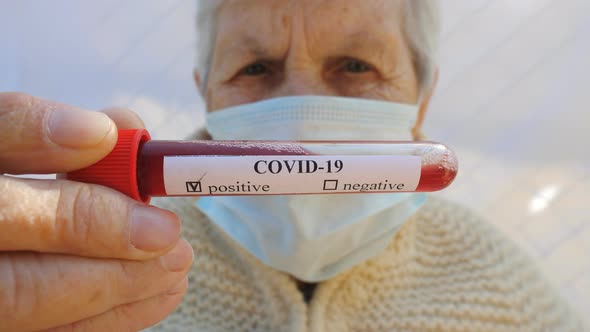 Old Lady with Protective Mask Holding Her Blood Test with Positive Result on Coronavirus. Sick