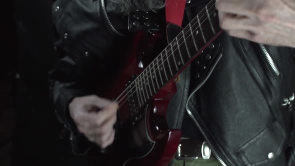 Close up rock musician hands plays on red electric guitar in leather jacket. Slow motion